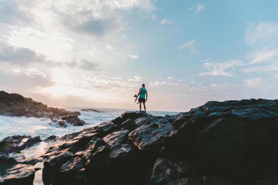 Free Image of Solitary figure with camera on rocky shore 