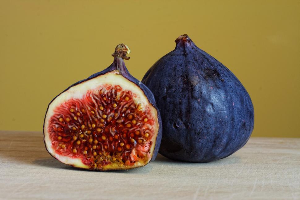 Free Image of Two figs, one cut open, on a wood surface 