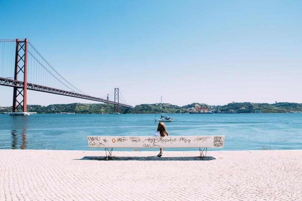 Free Image of Person sitting by river with bridge 