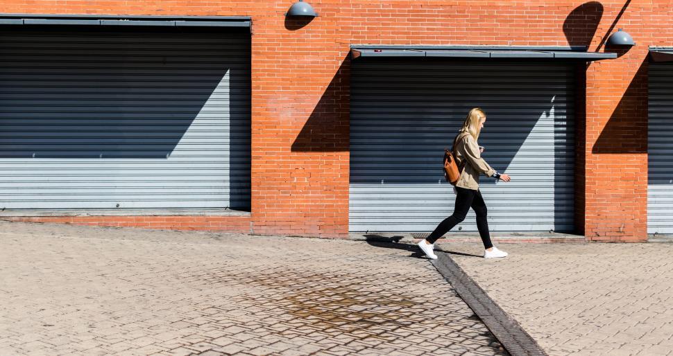 Free Image of Woman walking by brick wall with shadows 