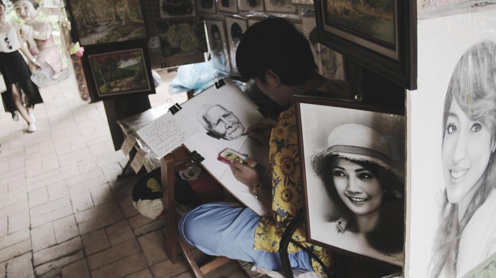 Free Image of Artist sketching portraits at market stall 