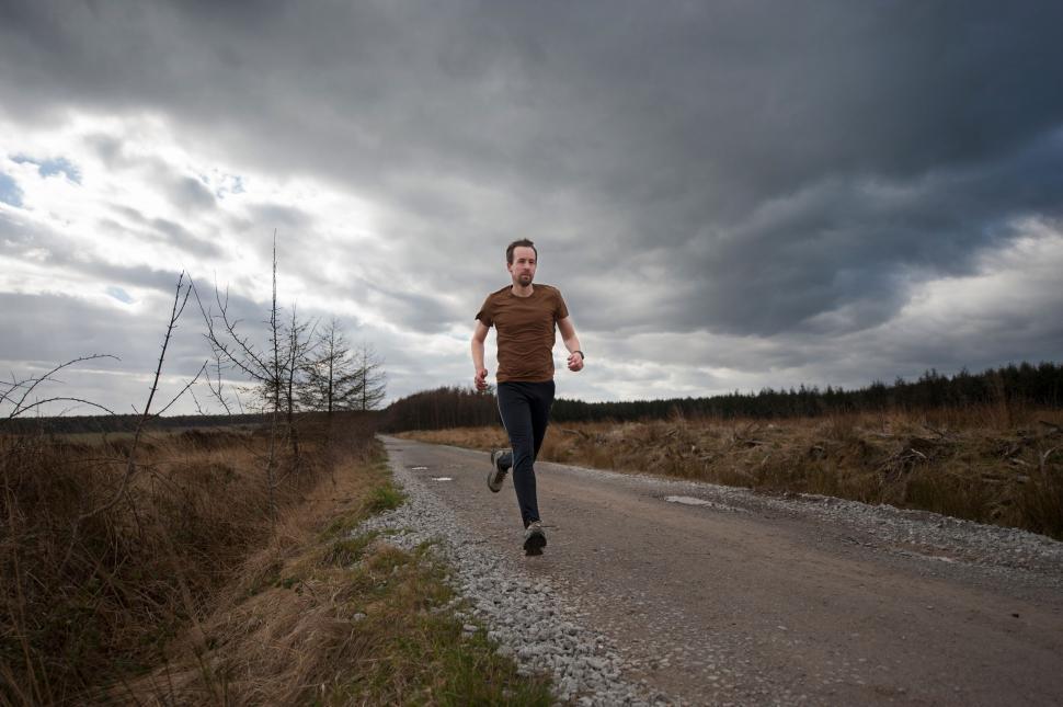 Free Image of Man running on cloudy countryside path 
