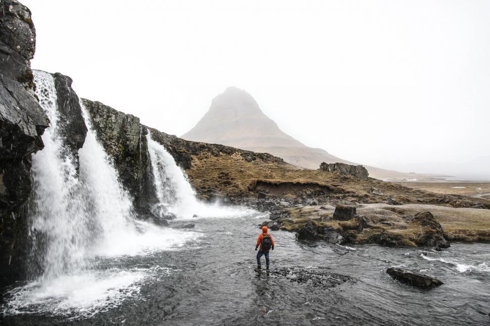 Free Image of Hiker by a waterfall with a mountain backdrop 