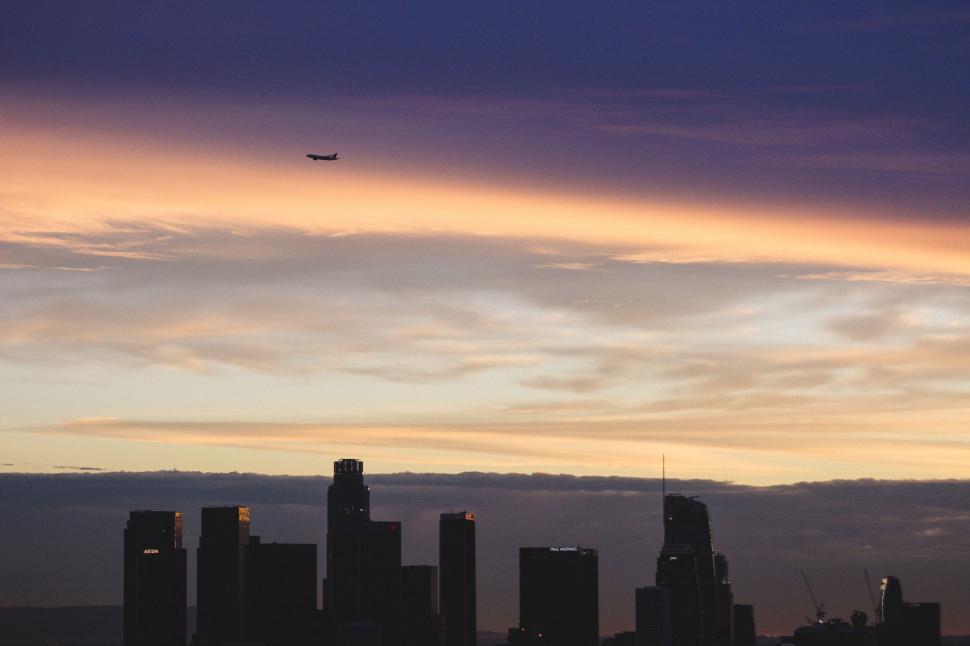 Free Image of Sunset sky over cityscape with airplane 