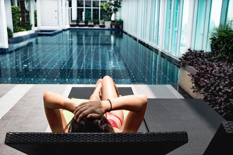 Free Image of Woman relaxing by a luxury hotel pool 