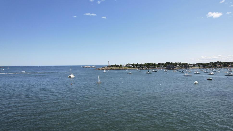 Free Image of Busy coastal harbor with boats, lighthouse and blue sky 