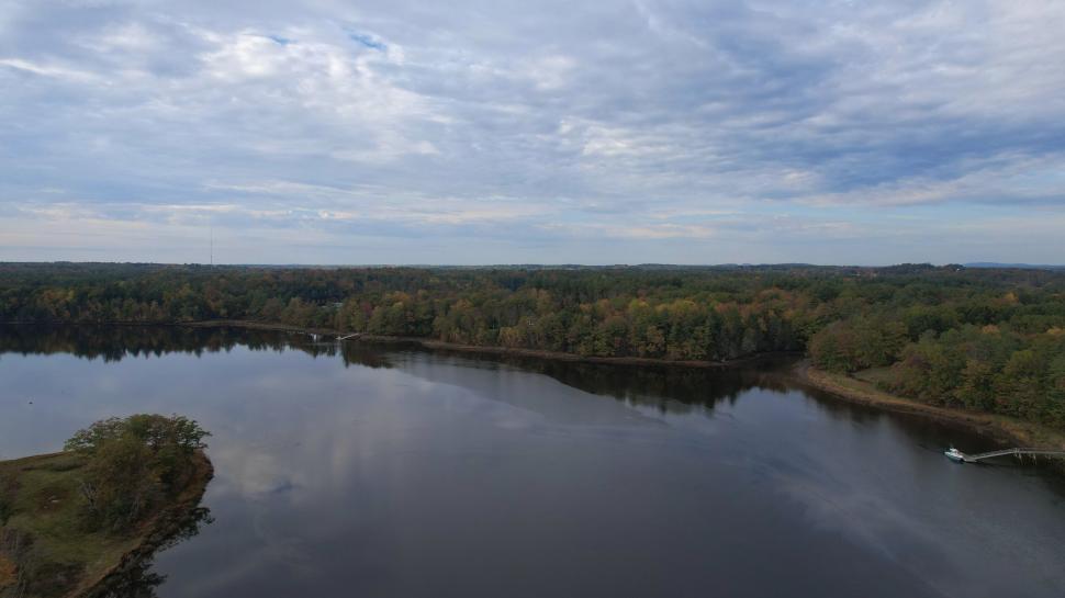 Free Image of Calm lake with forested shoreline under cloudy skies 