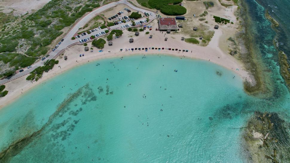 Free Image of Aerial view of turquoise beach with cars and buildings 