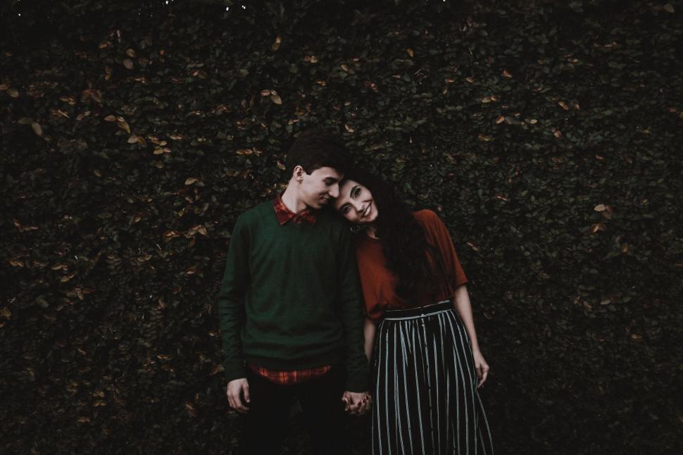 Free Image of Couple holding hands in front of green foliage wall. 