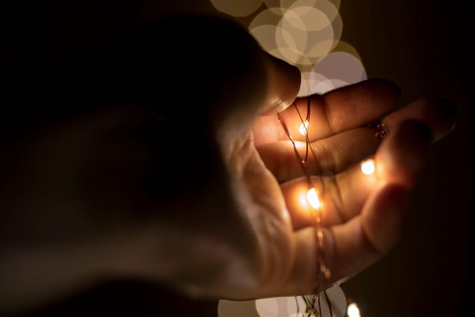 Free Image of Hand gently holding small lights in a dark setting 