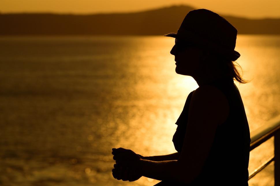 Free Image of Person in Hat Silhouetted Against Golden Sunset Over Water 