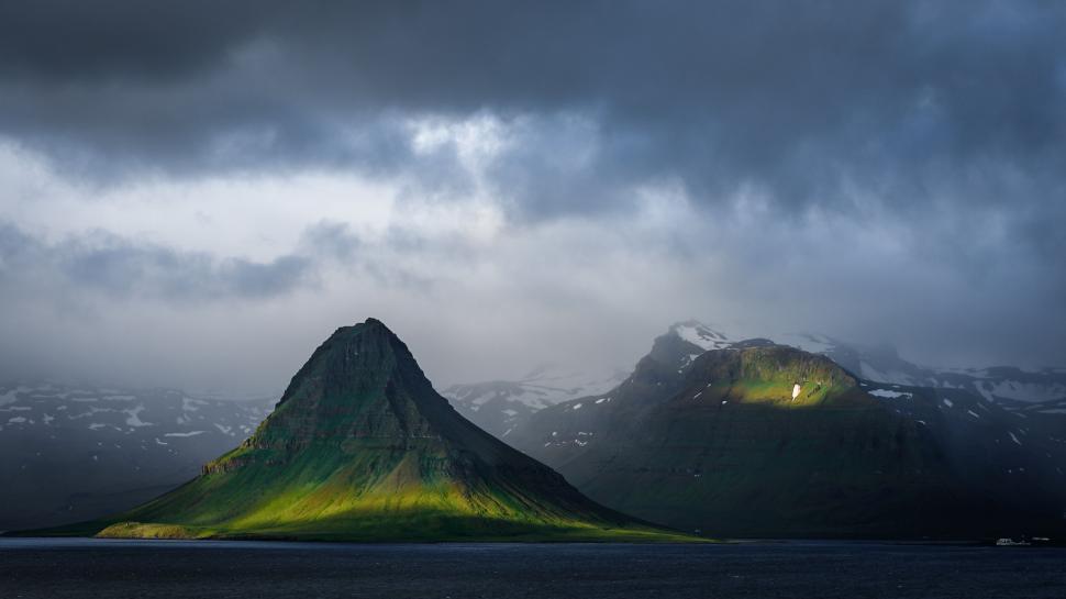 Free Image of Sunlight breaking through dramatic clouds over mountain. 