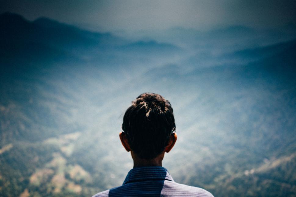 Free Image of Man standing on mountain overlooking misty valley 