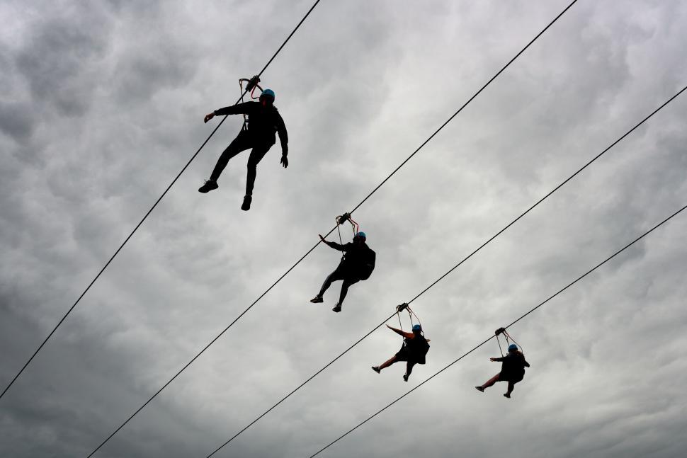 Free Image of Adventure seekers ziplining through cloudy sky. 