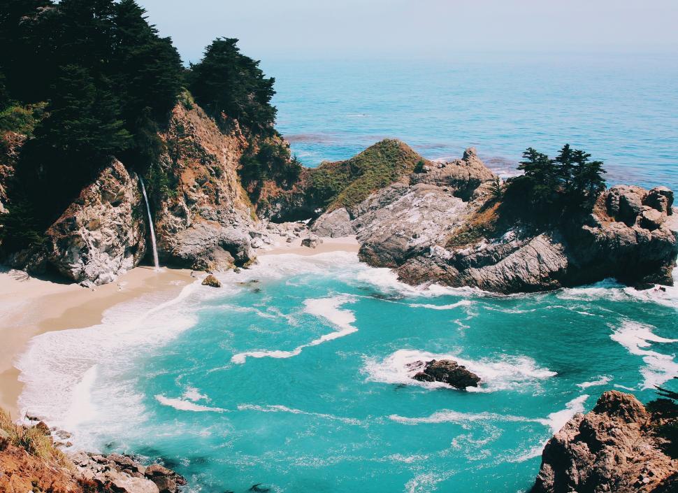 Free Image of Turquoise cove with waterfall surrounded by rocky cliffs 