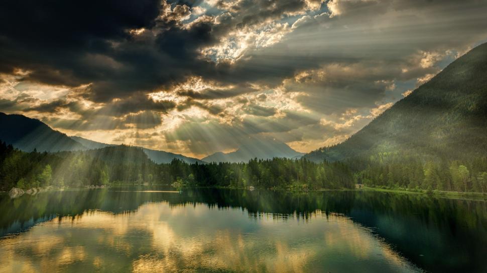 Free Image of Sunbeams over a serene lake surrounded by mountains 