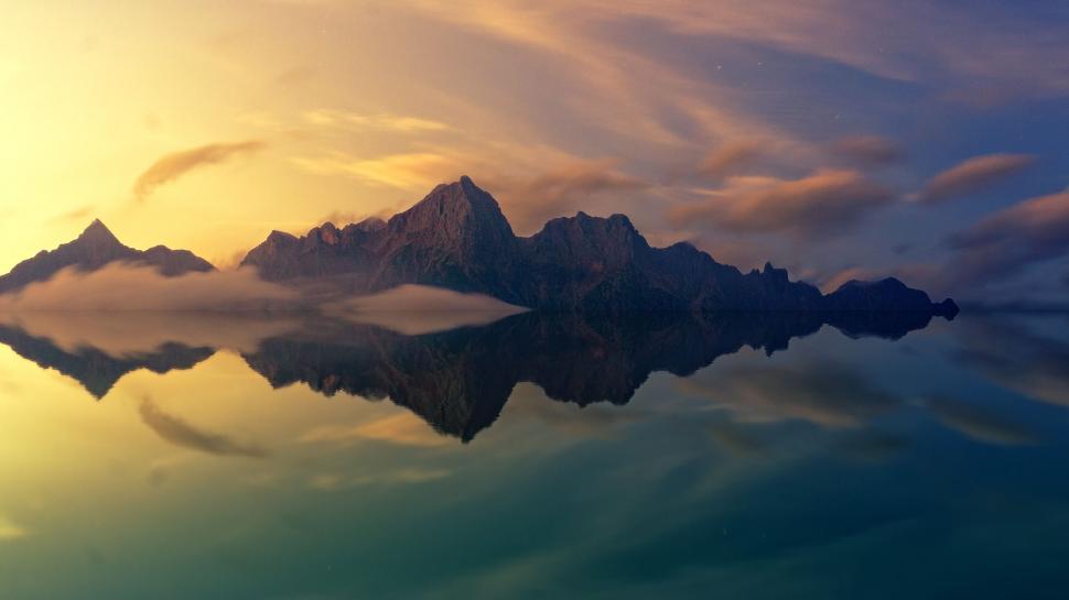 Free Image of A serene lake mirroring rugged mountains at dawn 