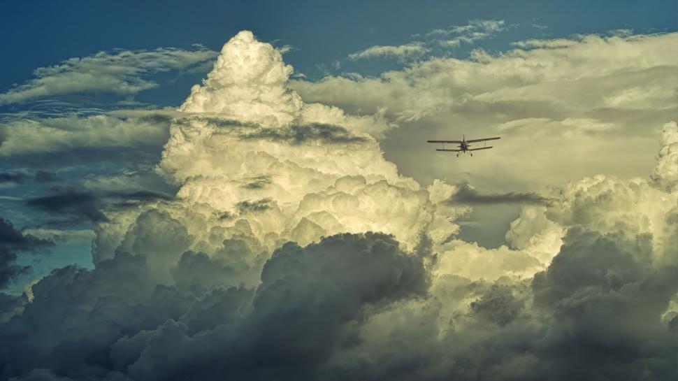 Free Image of Airplane flying amongst massive clouds and blue sky 
