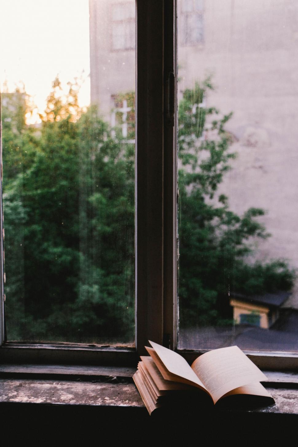 Free Image of Open book on a windowsill with a view of dusky sky. 