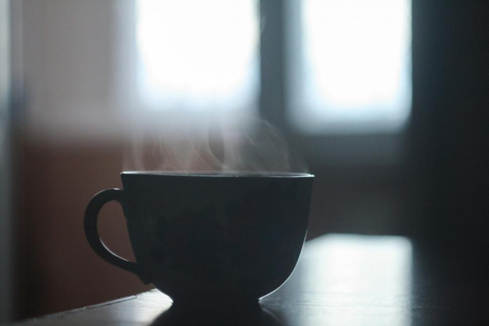 Free Image of Steaming cup of coffee on a dark table near windows. 