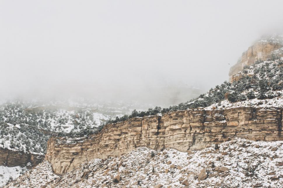 Free Image of Rocky cliff with snow-covered landscape under cloudy sky. 