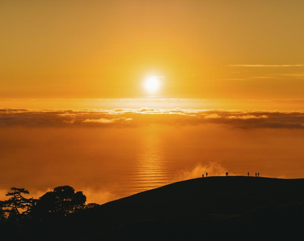 Free Image of Silhouetted figures on hill at sunset with orange sky. 