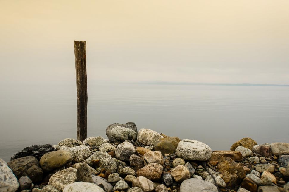 Free Image of Tranquil lakeside with rocks and single standing log 