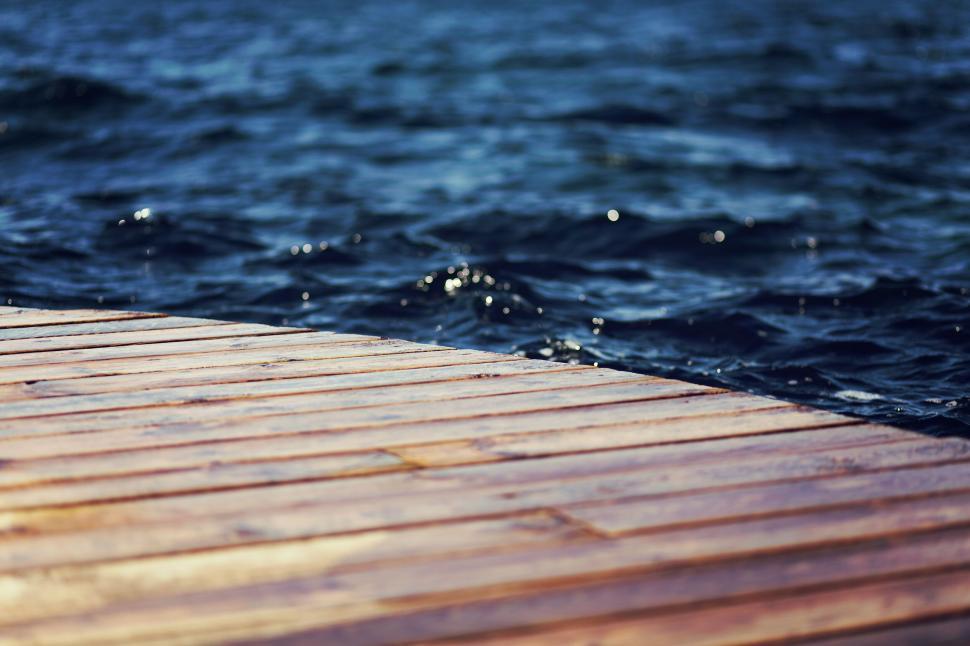 Free Image of Wooden dock extending over the calm, rippling water 