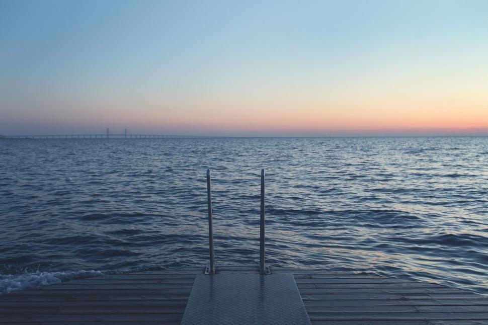 Free Image of Metal ladder leading down to the calm ocean at sunset. 