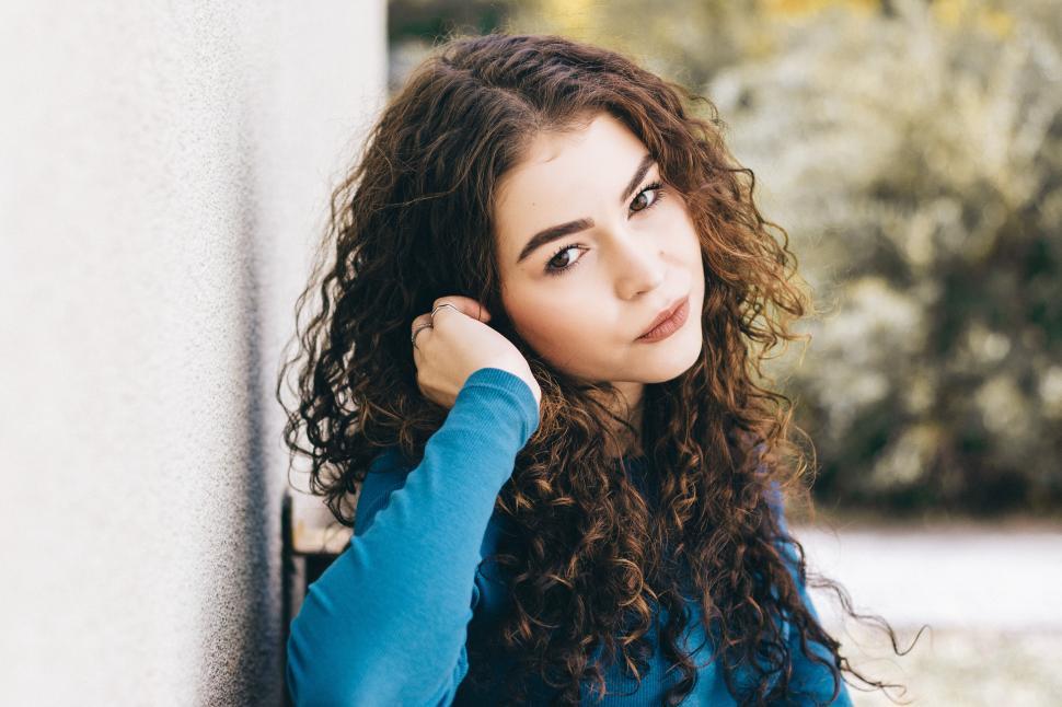 Free Image of Curly-haired person leaning against wall outdoors. 