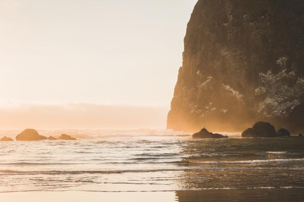 Free Image of Sunset at rocky beach with large cliff and calm waves. 