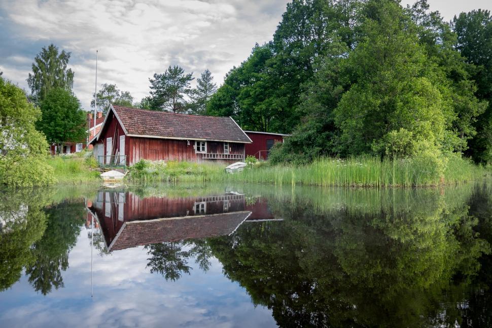 Free Image of Rustic red house with lush greenery and reflective pond 