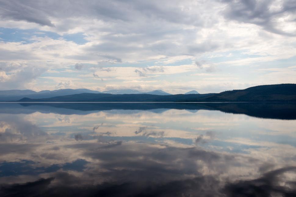 Free Image of Calm lake reflecting sky with clouds and mountains 