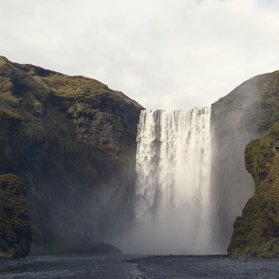 Free Image of A tall waterfall cascading between green cliffs 