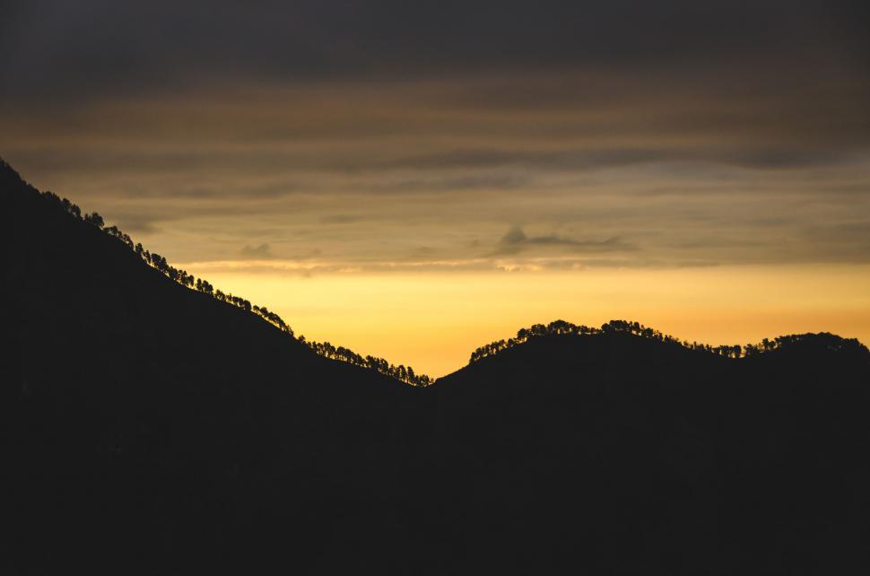 Free Image of Golden sunset over silhouette hills with trees. 