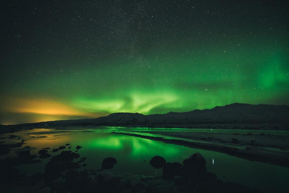 Free Image of The Northern Lights reflected over calm waters by night. 