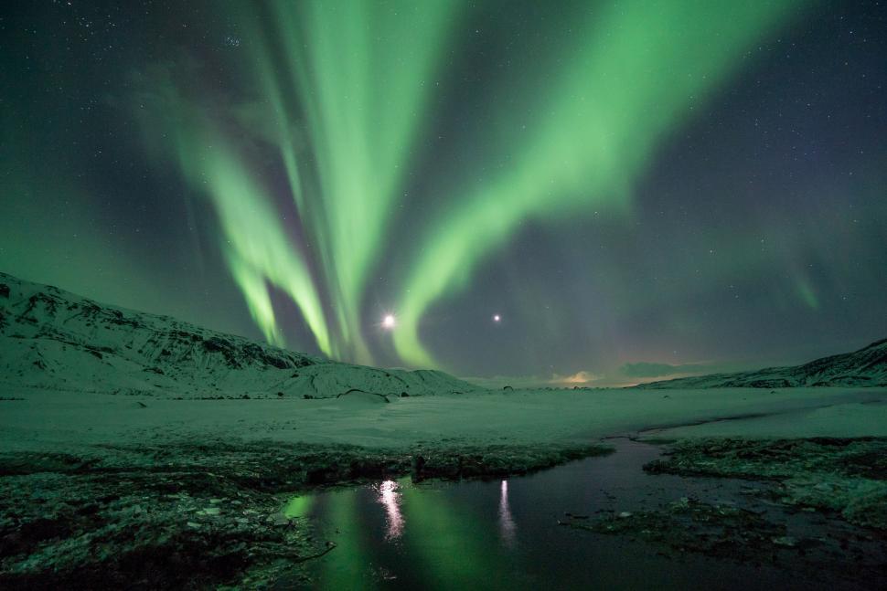 Free Image of Aurora borealis dancing in night sky over snow-covered land. 