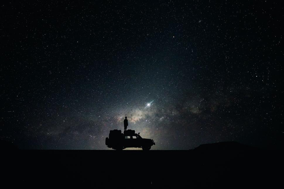 Free Image of Person stands on vehicle roof under starry night sky 