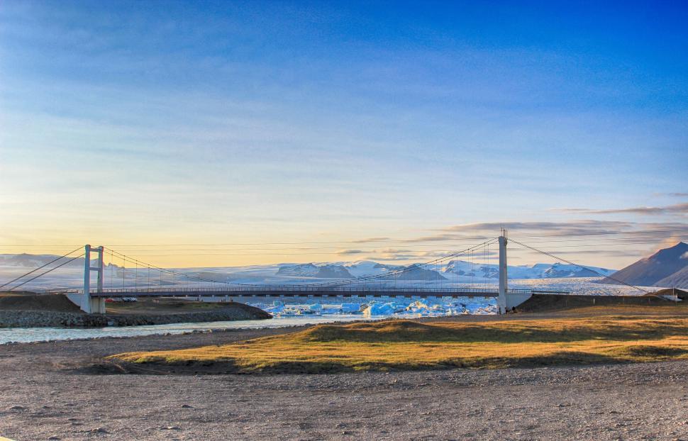 Free Image of Suspension bridge over a river with a mountainous backdrop. 
