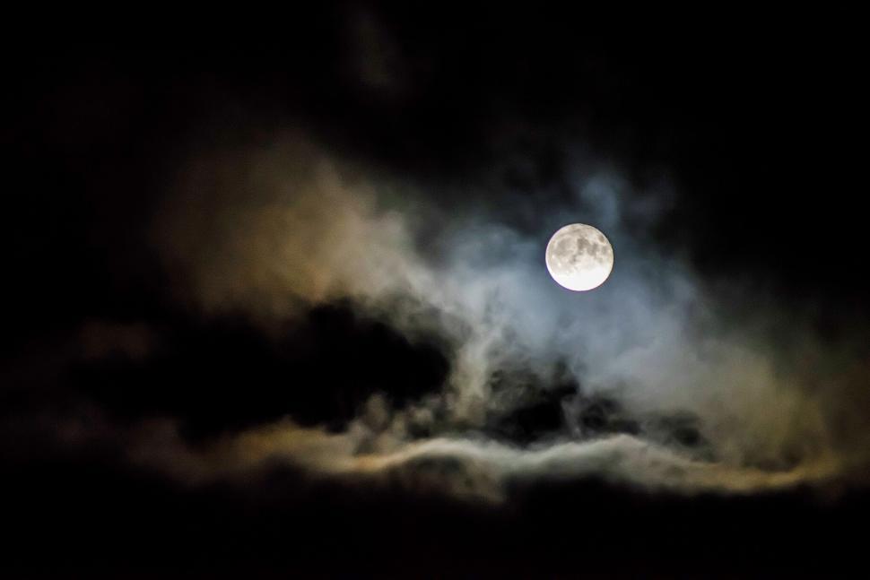 Free Image of Full moon shines brightly through a dramatic cloudy sky 