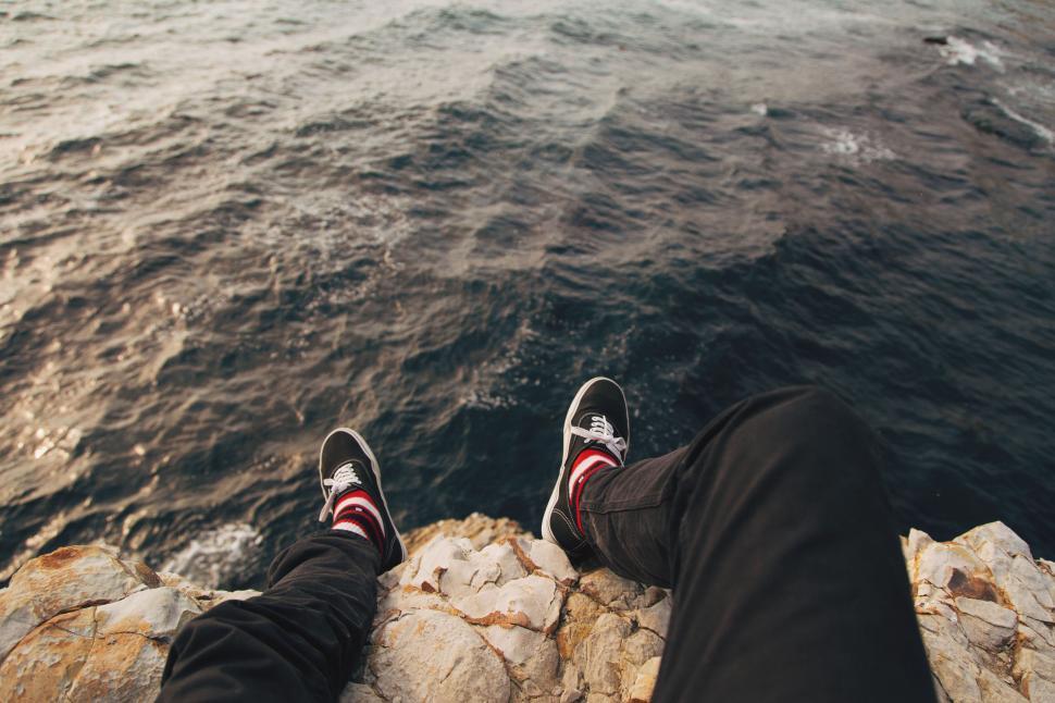 Free Image of Pair of legs and shoes above rocky edge overlooking sea 