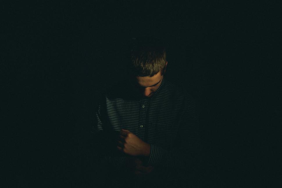 Free Image of Man in dim light with striped shirt looking downwards 