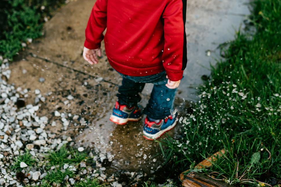 Free Image of Child in red jacket splashing water on a rainy day. 