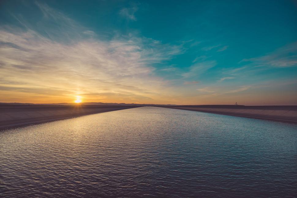 Free Image of Sun setting over a vast calm water body and horizon 