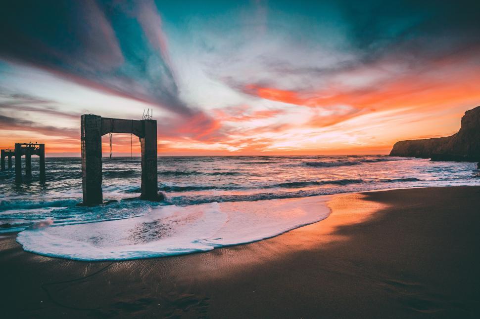 Free Image of Sunset over the ocean with waves and old pier remains. 