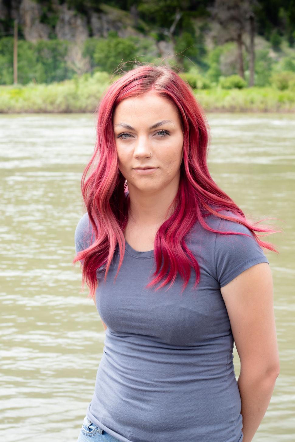 Free Image of Woman with red hair standing near river, natural scenery 