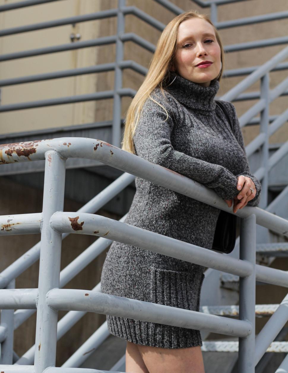 Free Image of Woman in gray turtleneck dress by metal staircase 