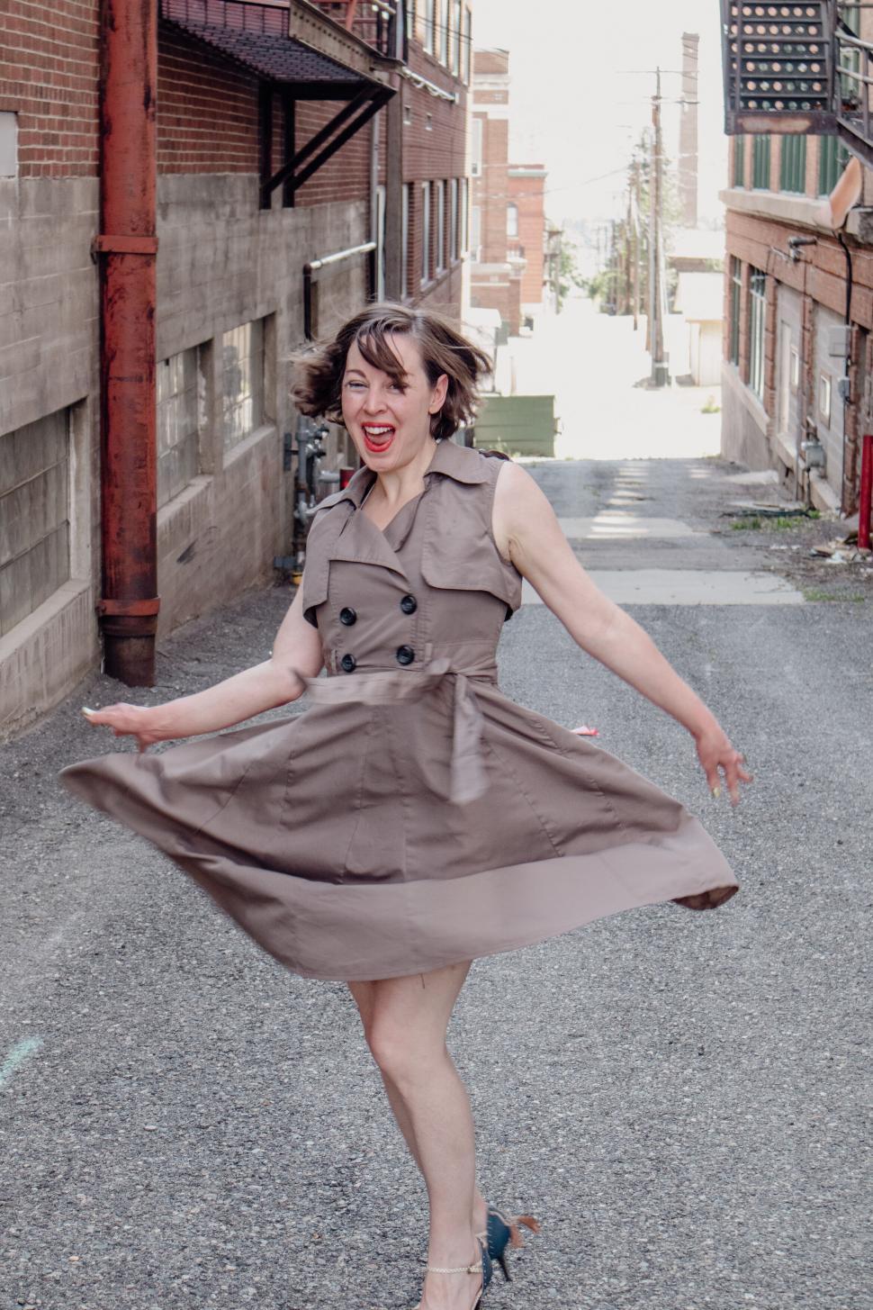 Free Image of Woman twirling in beige dress in urban alleyway 