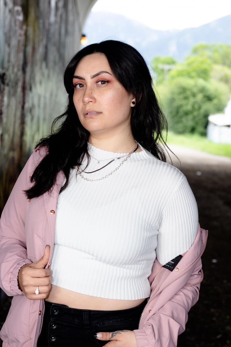 Free Image of Young woman in white top and pink jacket outdoors 