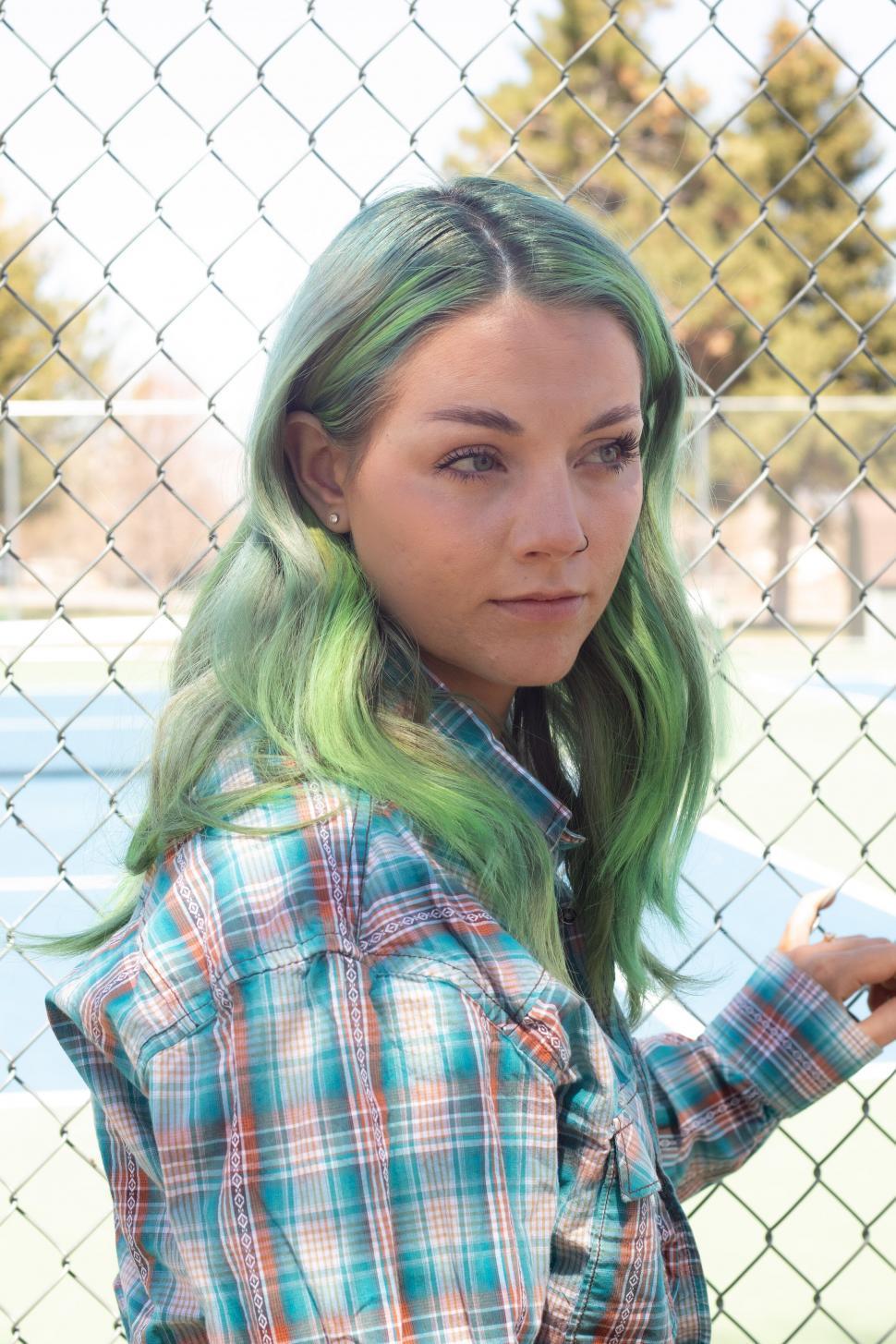 Free Image of Woman with green hair and plaid shirt by chain fence 
